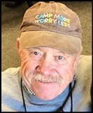 A senior wearing a brown cap with colorful embroidered text that reads “CAMP MORE WORRY LESS" and smiling. Description generated by AI