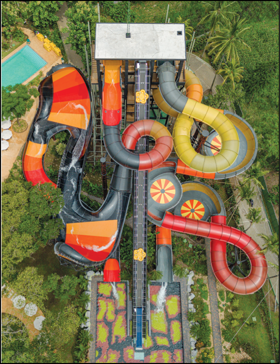 Aerial view of a colorful water slide complex with multiple twisting and looping slides surrounded by greenery and a nearby swimming pool. Description generated by AI