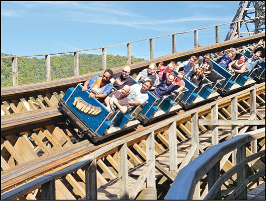 A group of people are riding a wooden roller coaster named Twister on a sunny day with a clear blue sky. Description generated by AI