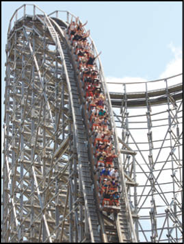A large group of people wearing casual clothing are riding a wooden roller coaster as it descends a steep track under a clear sky. Description generated by AI