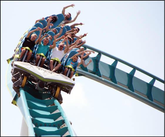 A group of people with raised hands are riding a roller coaster as it descends a steep track. Description generated by AI
