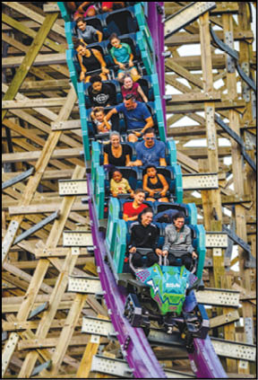 A group of people seated in a roller coaster car are descending a wooden track with expressions of excitement and joy. Description generated by AI