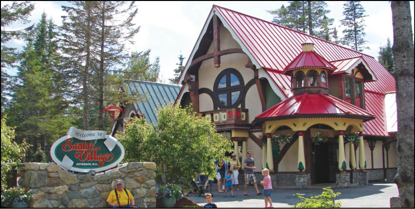 A festive village scene with a decorative building featuring a red roof and a sign that reads “Welcome to Santa's Village" surrounded by trees and people walking nearby. Description generated by AI