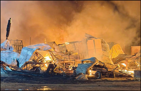 A large structure made of metal and wood is collapsing and engulfed in flames with thick smoke rising into the night sky. Description generated by AI